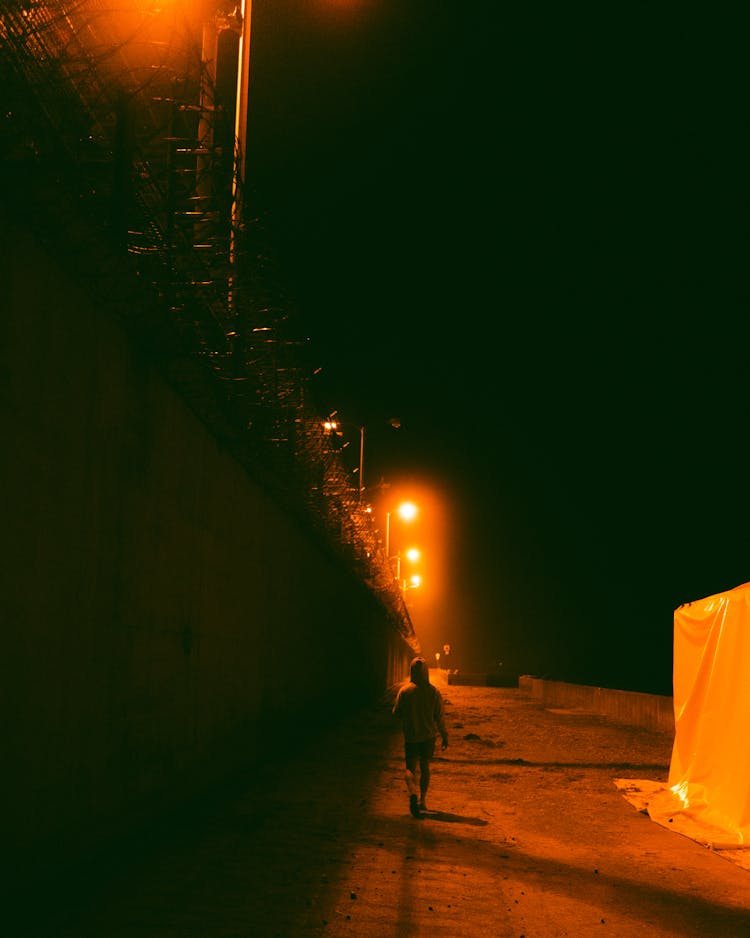 Unrecognizable Person Walking Along Stone Wall In Night City