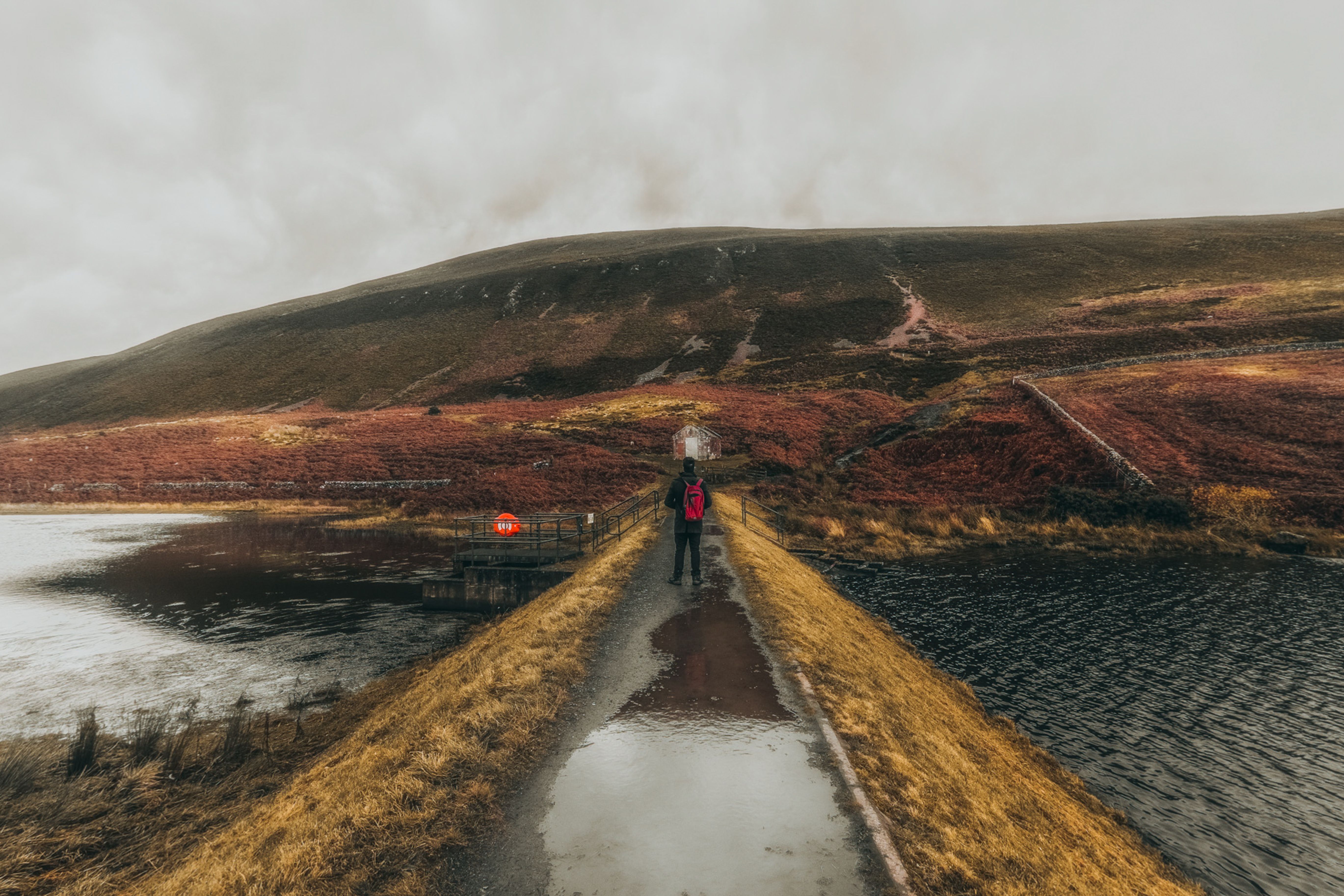 A lone traveler crosses a bridge in the autumnal Scottish Highlands, enveloped in mist.