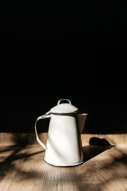 Old fashioned white metal kettle placed on empty wooden table against black background