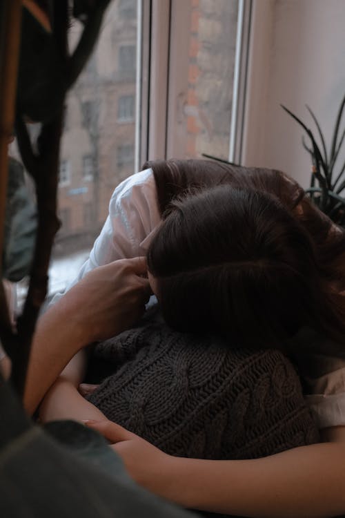 Unrecognizable romantic couple hugging and touching face gently while resting together on windowsill in daylight