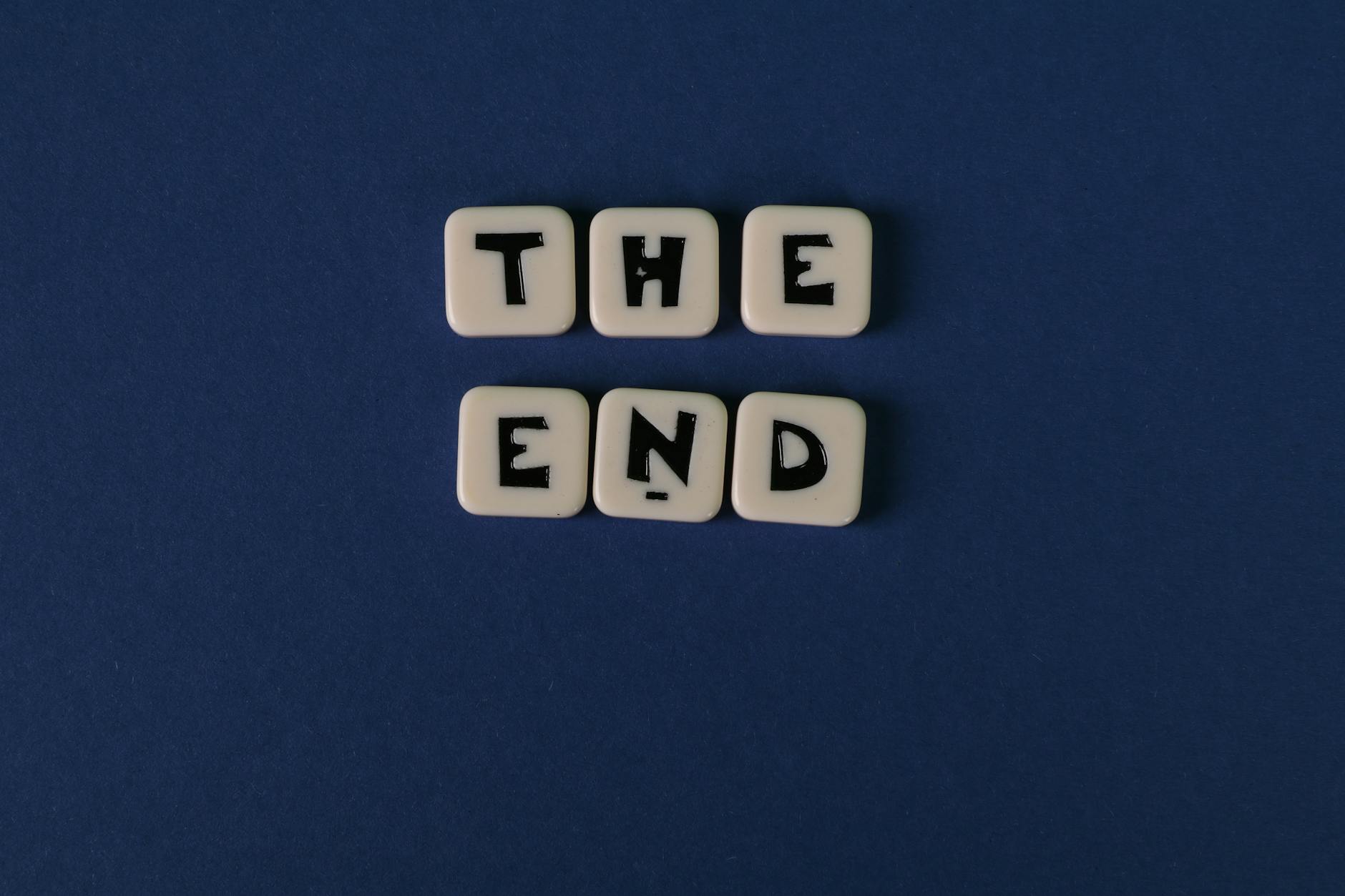 Scrabble tiles spelling 'The End' on a minimalist blue background. Perfect for conceptual designs.