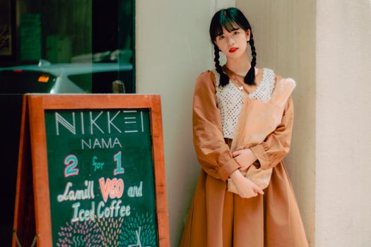 Calm young Asian female with braids in stylish outfits standing near cafe entrance with package of fresh bread in hands