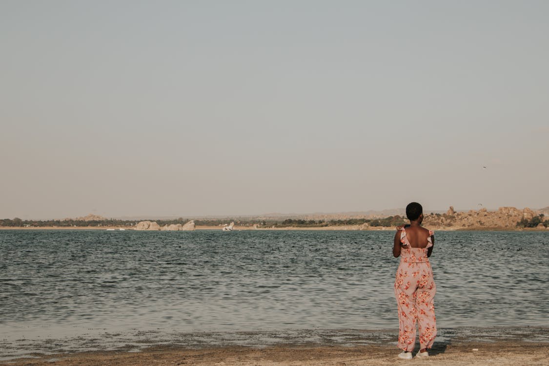 Back View of a Woman in a Floral Jumpsuit Standing on the Seashore