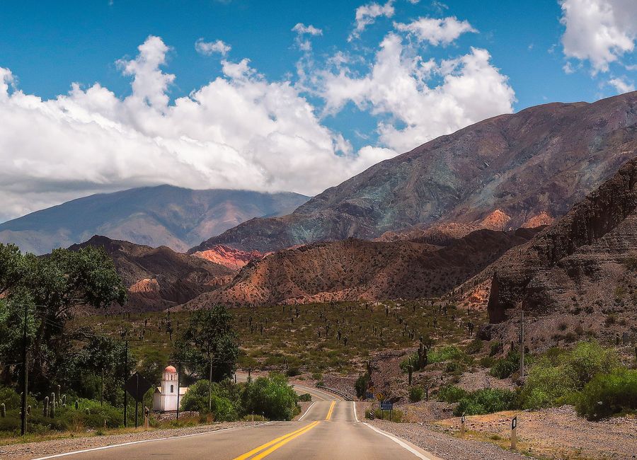 A picturesque view of a winding road through mountains under a bright blue sky with fluffy clouds.