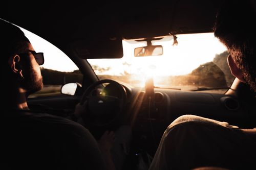 Free Two men driving in a car interior, enjoying a scenic view with sunlight streaming through the windshield. Stock Photo