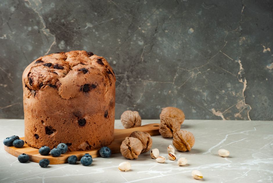 Pão artesanal de fermentação natural acompanhado de frutas secas e castanhas, sobre superfície de mármore com fundo texturizado.