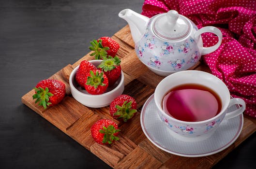 A cozy tea setup with a floral teapot and fresh strawberries arranged on a wooden tray.