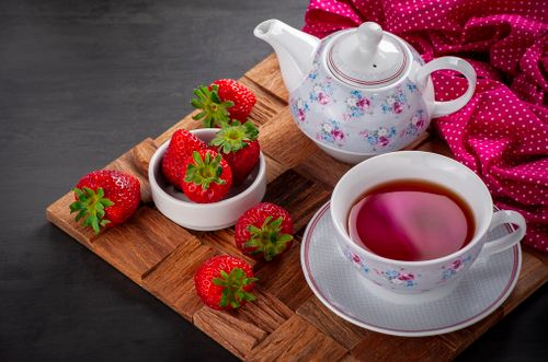 Free A cozy tea setup with a floral teapot and fresh strawberries arranged on a wooden tray. Stock Photo