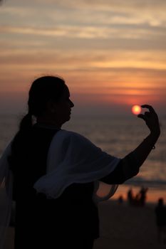 Artistic silhouette of a woman holding the sun at Maravanthe Beach sunset.