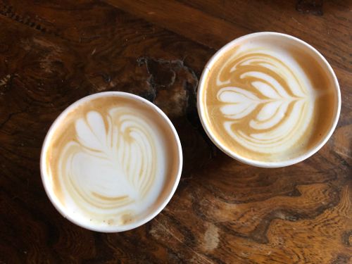Free Two beautifully crafted lattes with intricate art on a rustic wooden table. Perfect coffee shot for beverage enthusiasts. Stock Photo