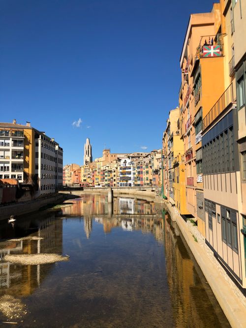 Free Capture of Girona's iconic riverside architecture reflected in the Onyar River under a clear blue sky. Stock Photo