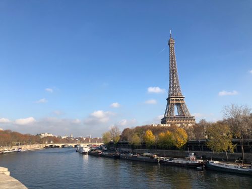 Free Scenic view of the Eiffel Tower near the Seine River with boats floating under a clear blue sky. Stock Photo