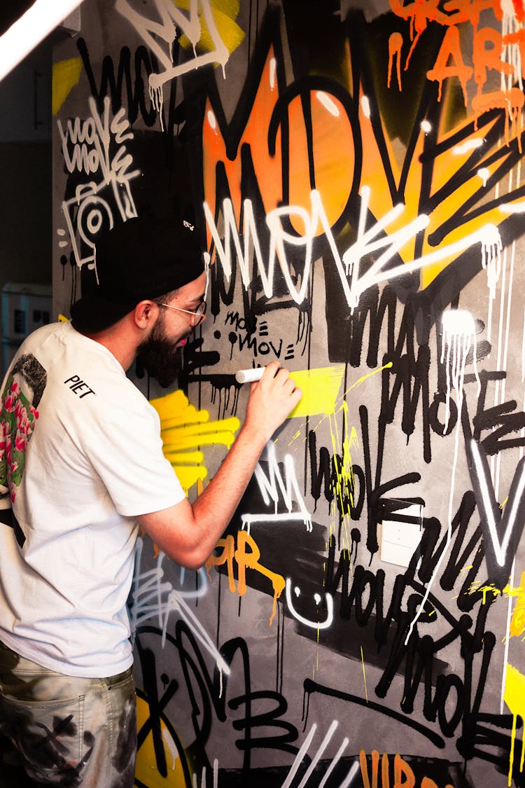 Man In A White Crew Neck Shirt Drawing On A Wall With Graffiti