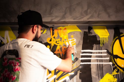 Photo of a Man in a Black Cap Spraying Paint on a Wall