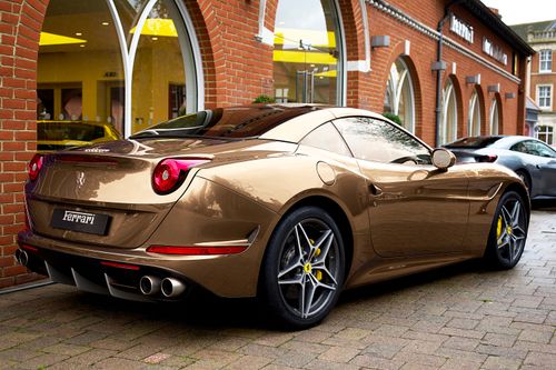 Free A sleek gold Ferrari sports car parked outdoors next to a brick building in England. Stock Photo