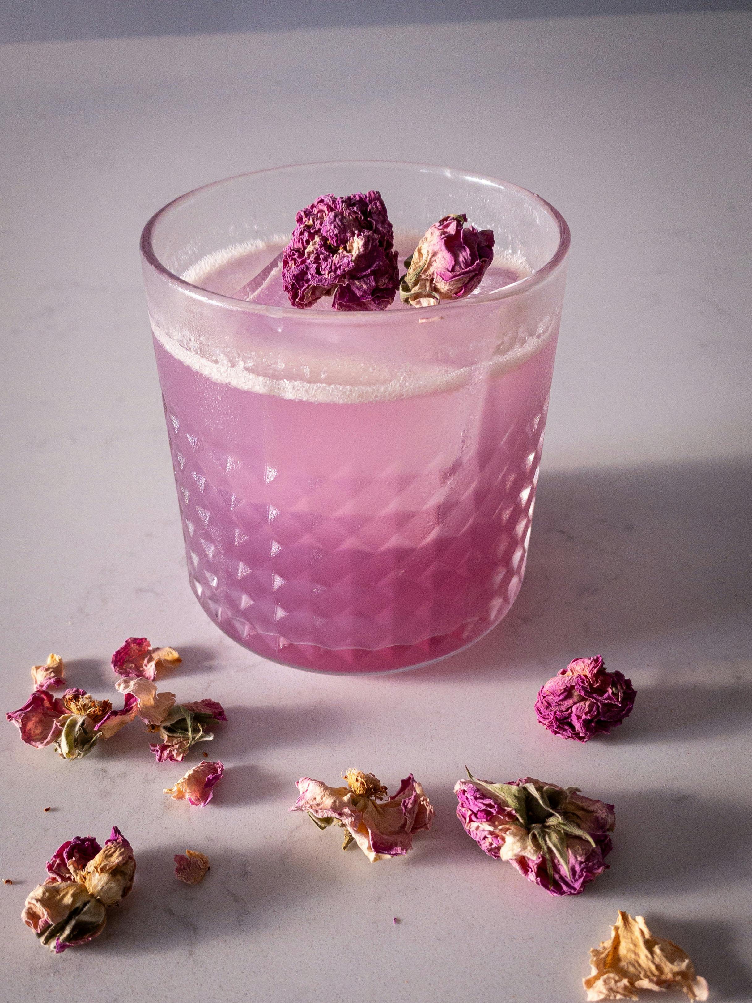 A refreshing pink cocktail adorned with dried rose petals on a white surface.