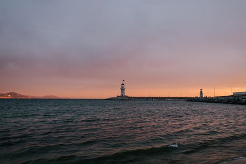 Free Picturesque scenery of rippling tranquil sea washing seacoast with white lighthouse under cloudy blue and pink sky at sundown Stock Photo