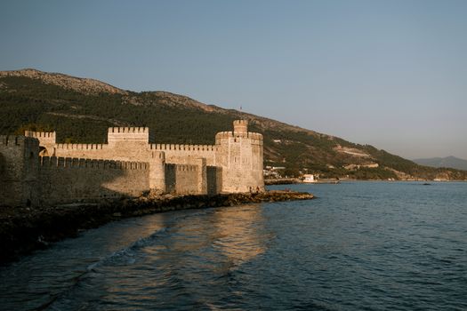 Facade of aged medieval Mamure Castle built on seashore near grassy lush hills under clear blue sky in Turkey
