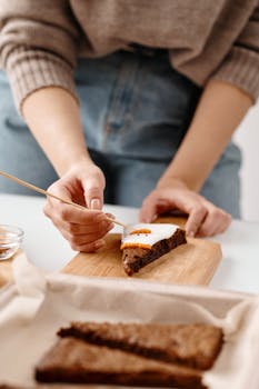 Close-up of hands decorating Christmas biscuits with icing on a wooden tray.