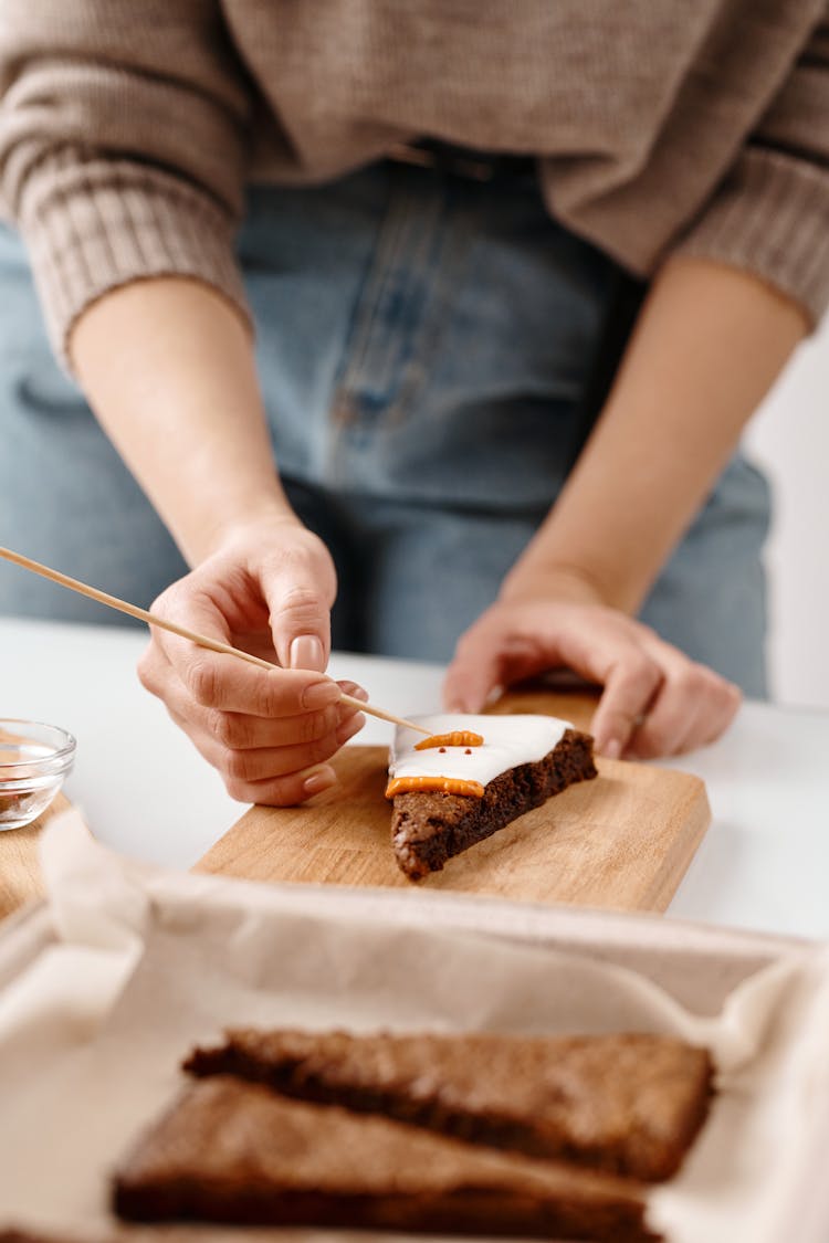 Person Decorating A Triangle Shaped Brown Cookie