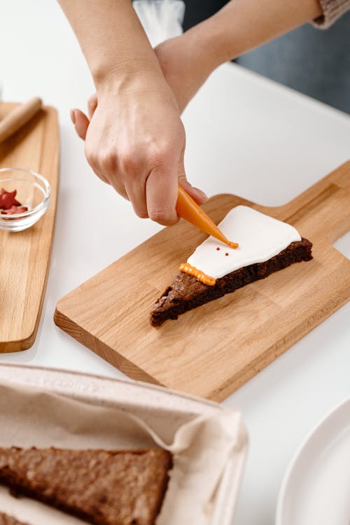 Person Decorating a Triangle Shaped Brown Cake