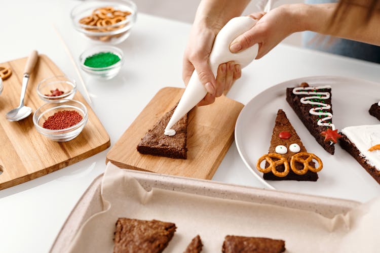 Person Decorating A Triangle Shaped Brown Cookie