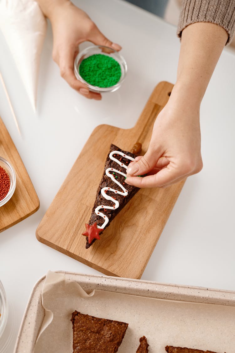 Person Decorating A Triangle Shaped Brown Cookie