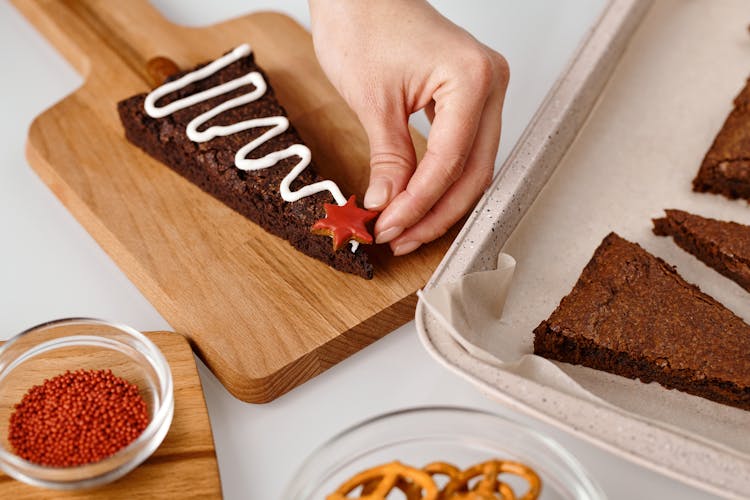 Person Decorating A Triangle Shaped Brown Cookie