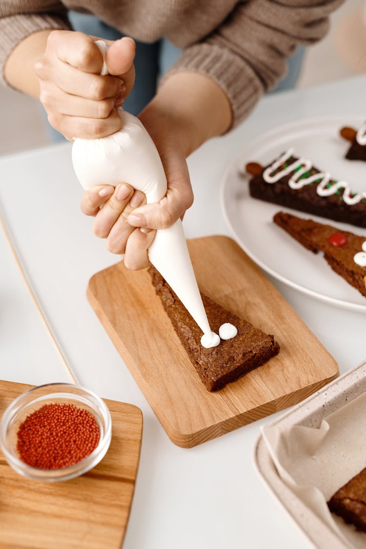 Person Decorating A Triangle Shaped Brown Cookie