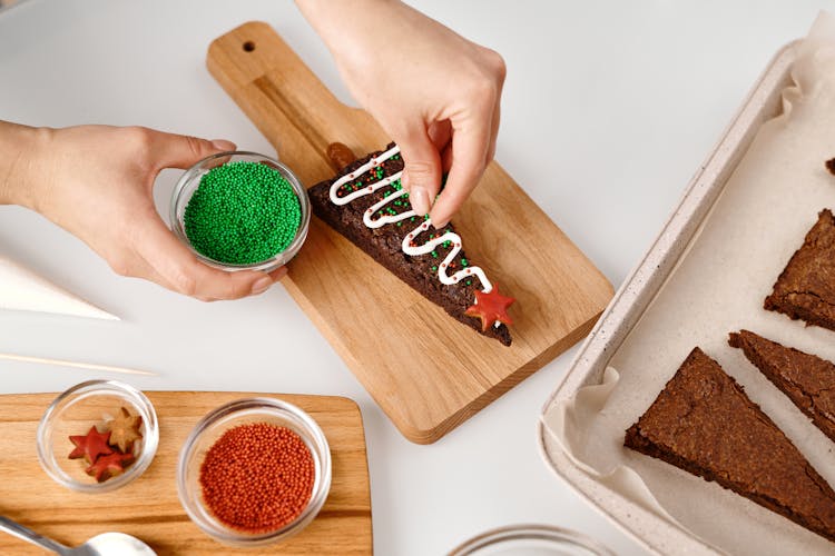 Person Decorating A Triangle Shaped Brown Cookie