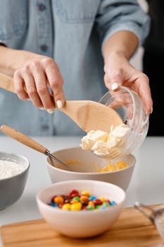 Close-up of hands adding butter for baking with colorful candies nearby.