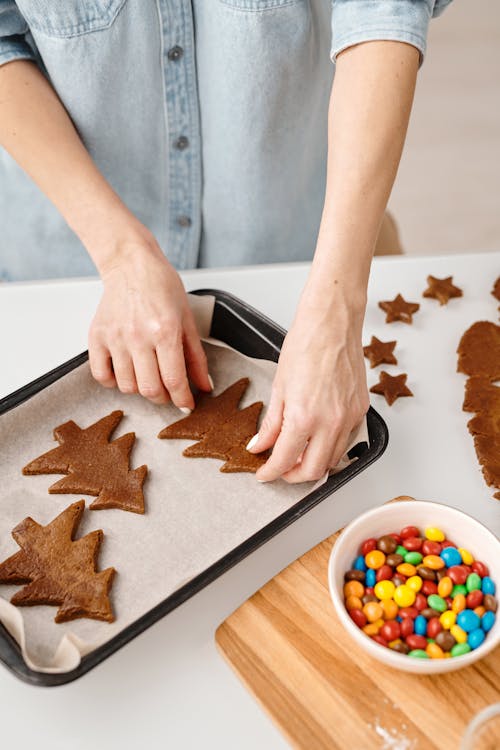 Person Putting Christmas Tree Shaped Cookies on a Tray