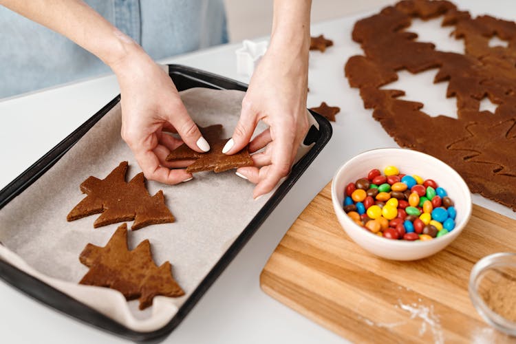 Person Putting Christmas Tree Shaped Cookies On A Tray