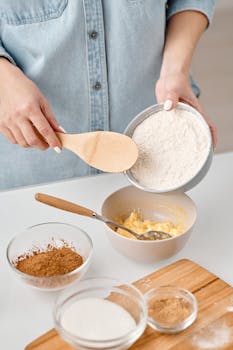 Hands preparing homemade cake batter with flour and spices in a kitchen setting.