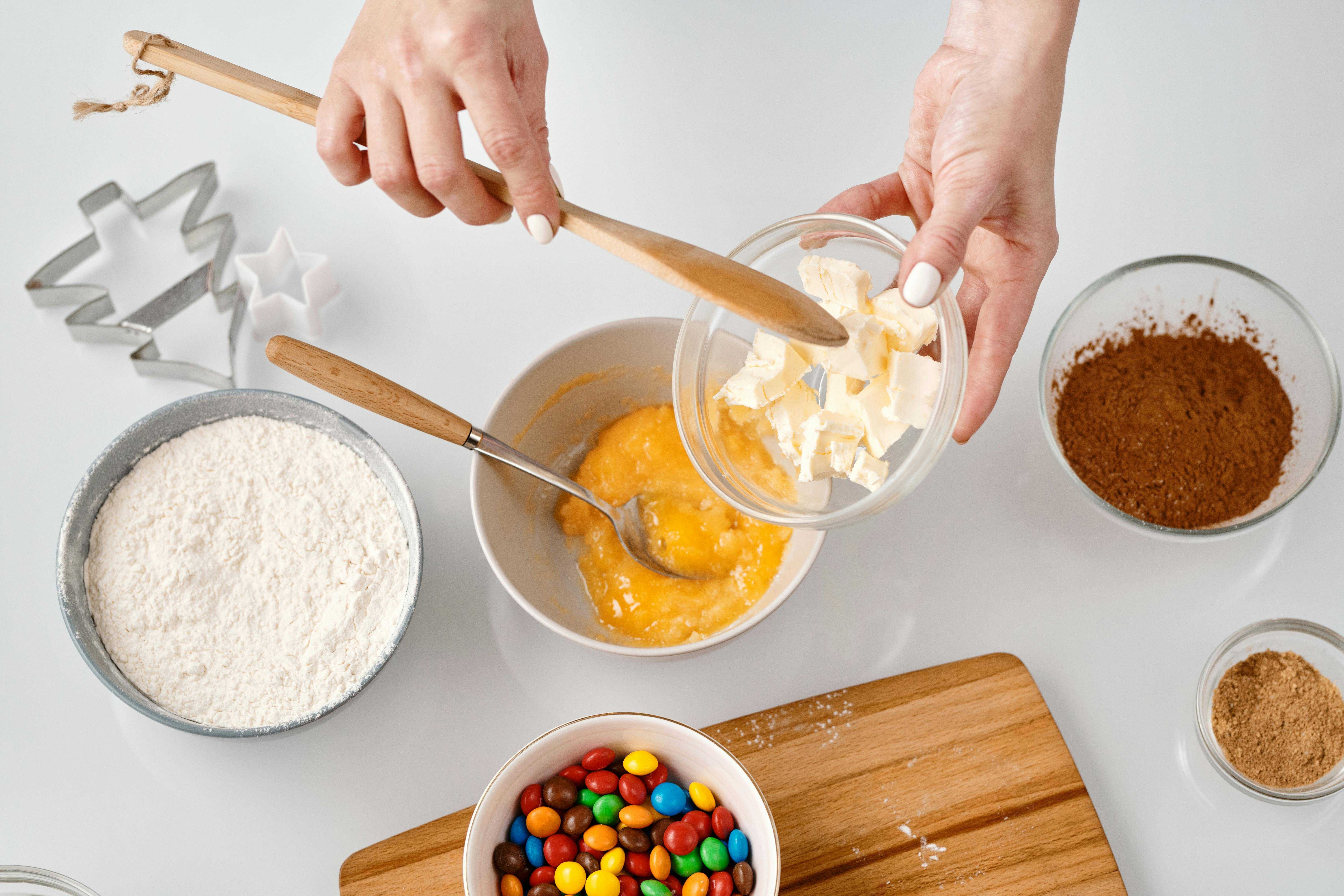 A person preparing ingredients for baking with a variety of bowls and colorful candies.