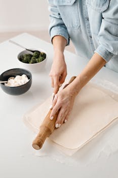 A person rolls dough on a countertop for homemade pastries with ingredients nearby.