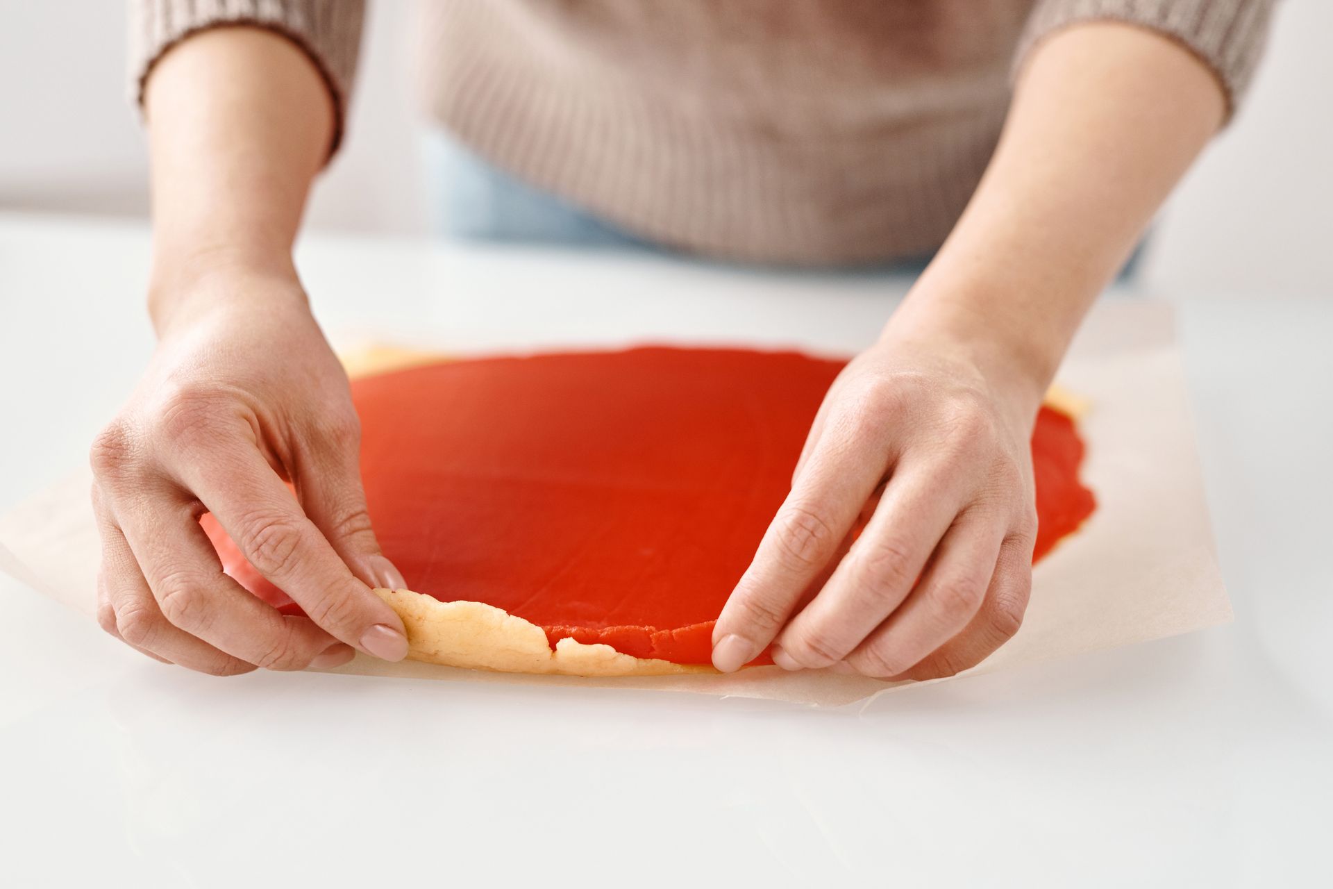 Close-up of hands preparing dough with wax paper for a homemade pastry.