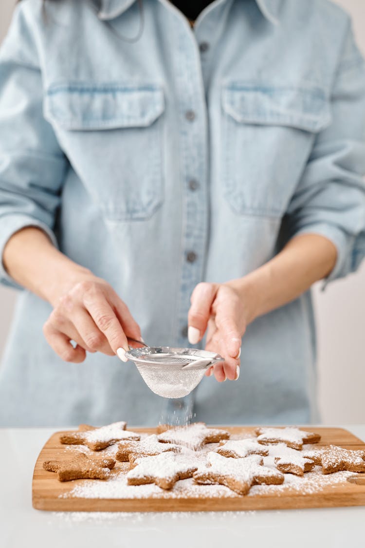 Person Using A Strainer To Sprinkle Sugared Powder On Brown Cookies