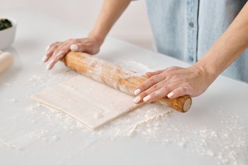 Free Hands rolling pastry dough on a floured surface with a wooden pin. Stock Photo