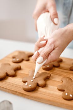 Hands decorating gingerbread cookies with icing during Christmas preparations.