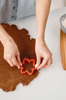 Adult hands using a red star cookie cutter to shape dough for holiday cookies.