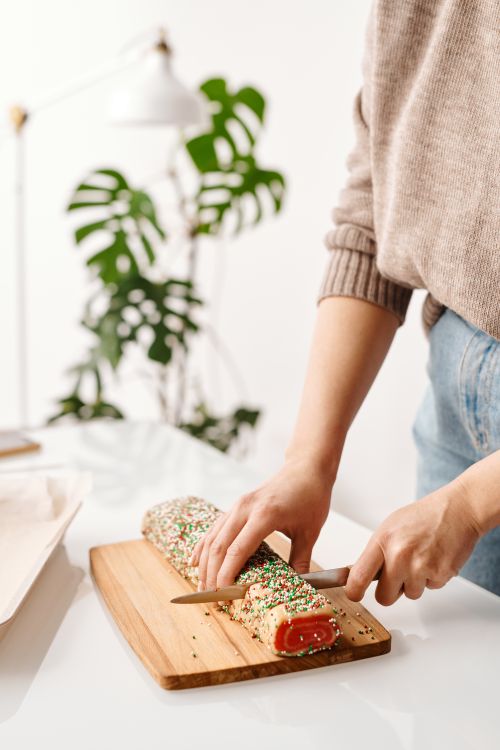 Free Close-up of a woman slicing a festive sprinkled cake on a wooden board indoors. Stock Photo