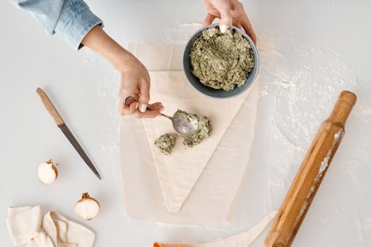 Woman preparing dough with herb filling for homemade pastry in modern kitchen.