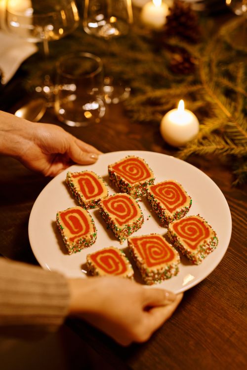 Free Plate of spiral Christmas cookies with colorful sprinkles, set on a wooden table surrounded by holiday decor. Stock Photo