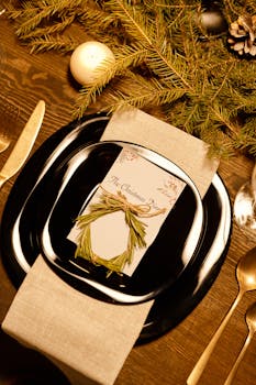 A stylish Christmas table setting featuring black dinnerware, gold cutlery, and holiday decor.
