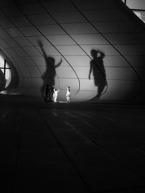 Children creating playful shadows on a modern architectural wall in Baku. Captured in black and white.