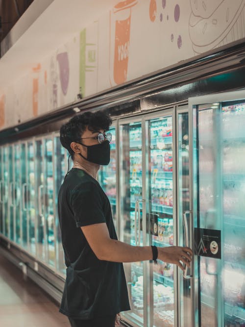 Man in mask opening supermarket fridge door