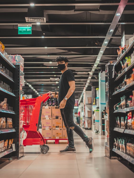 Man in mask pushing trolley in supermarket