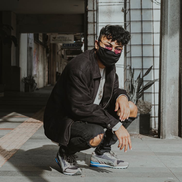 Stylish Ethnic Man In Mask Hunkering Down Near Parking Entrance