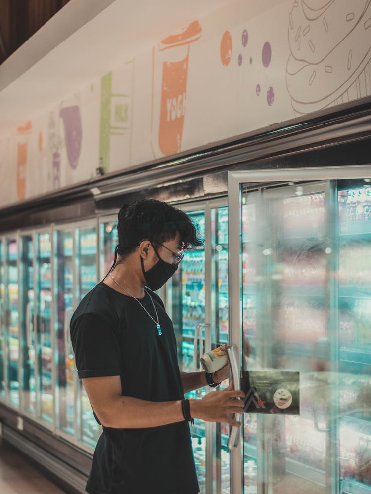 Man In Mask Choosing Products Presented On Fridge Shelf